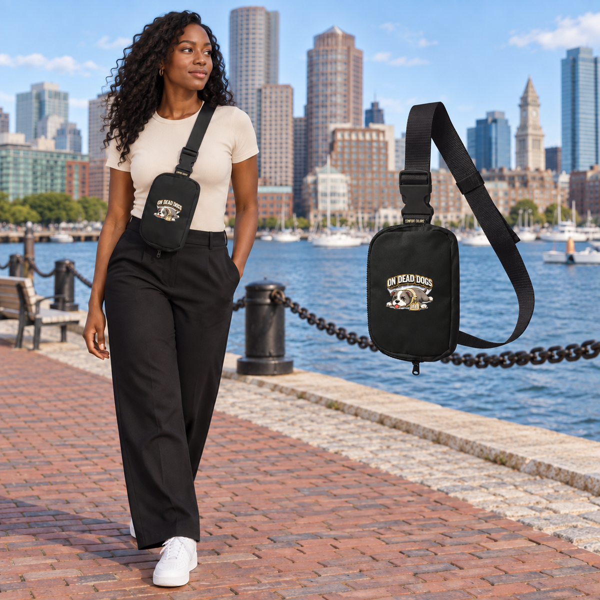 Black adult woman wearing the On Dead Dogs black sling bag at Boston waterfront with a matching floating bag at right.